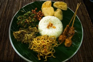 Plate of Balinese food with rice, satay, vegetables, peanuts, and noodles, showing local flavors tourists can try.