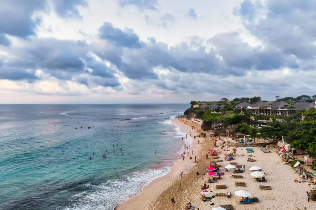 Wide beach in Nusa Dua with people swimming, walking, and relaxing along the coastline.