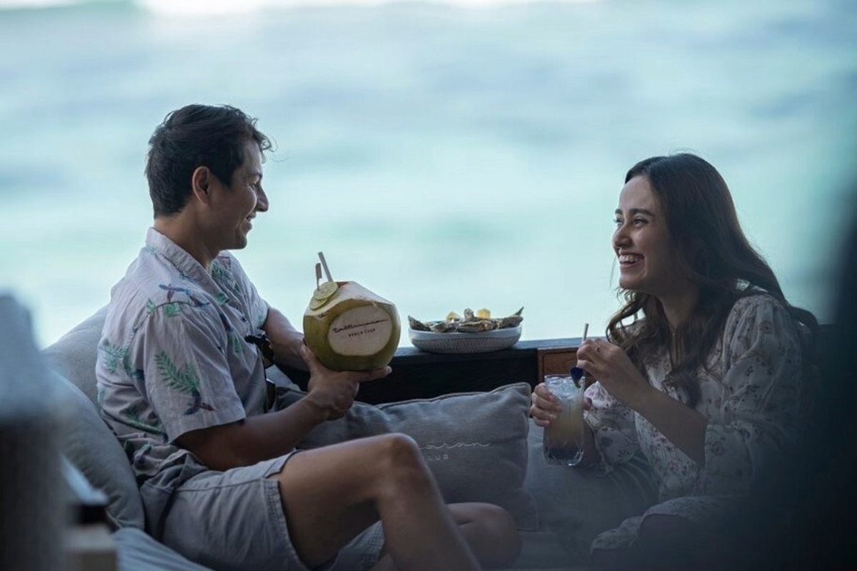 Couple relaxing by the ocean, drinking cocktails and coconut, enjoying a memorable beach club dining experience.