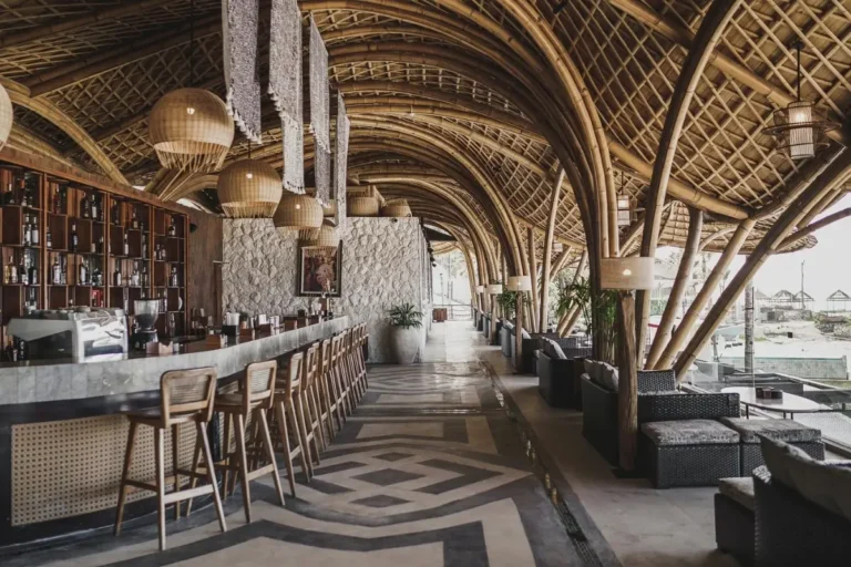 Open air beach club bar with bamboo roof, seating area, and ocean view in Bali.