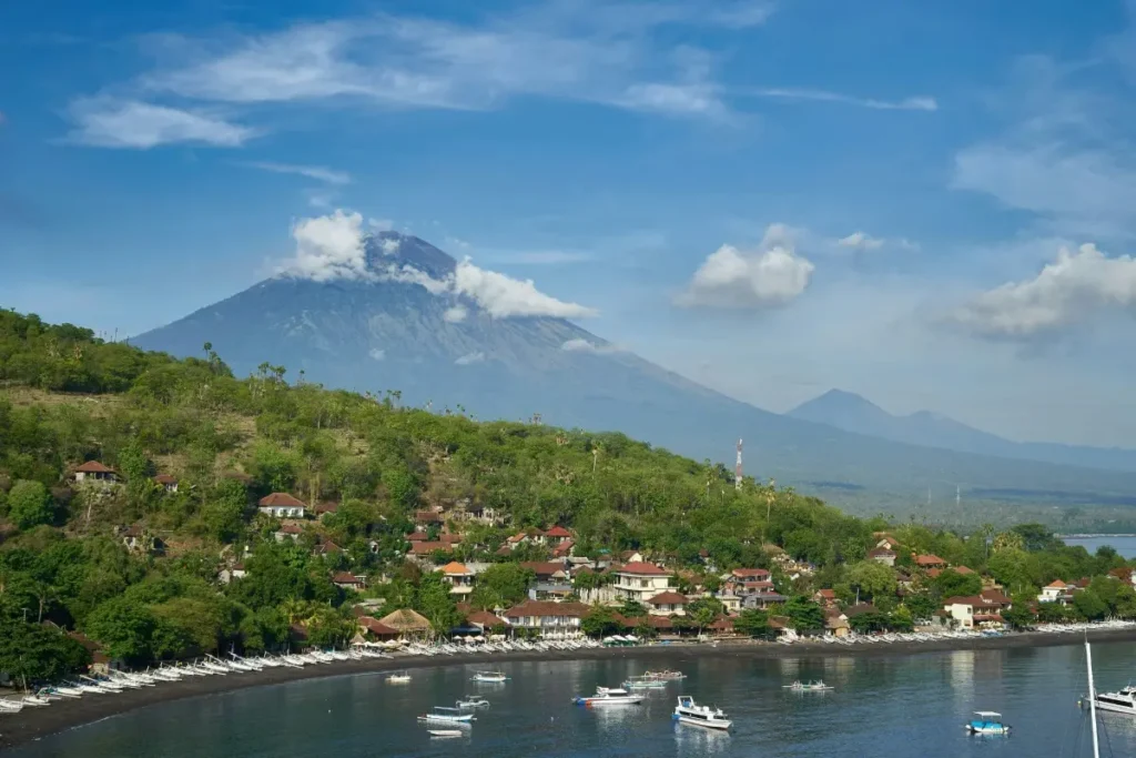 View of Amed coastline with Mount Agung, fishing boats, and a quiet village on Bali's eastern coast.