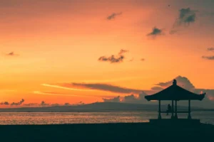Person sitting in a seaside pavilion, watching a Bali sunset over calm ocean waters.