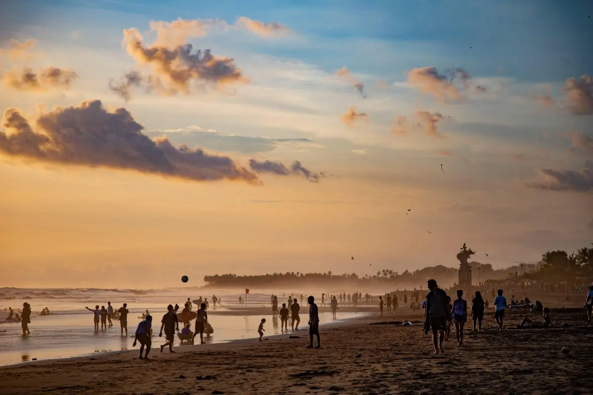 Visitors relax, walk, and play along a busy Bali beach at sunset during a beach day tour.